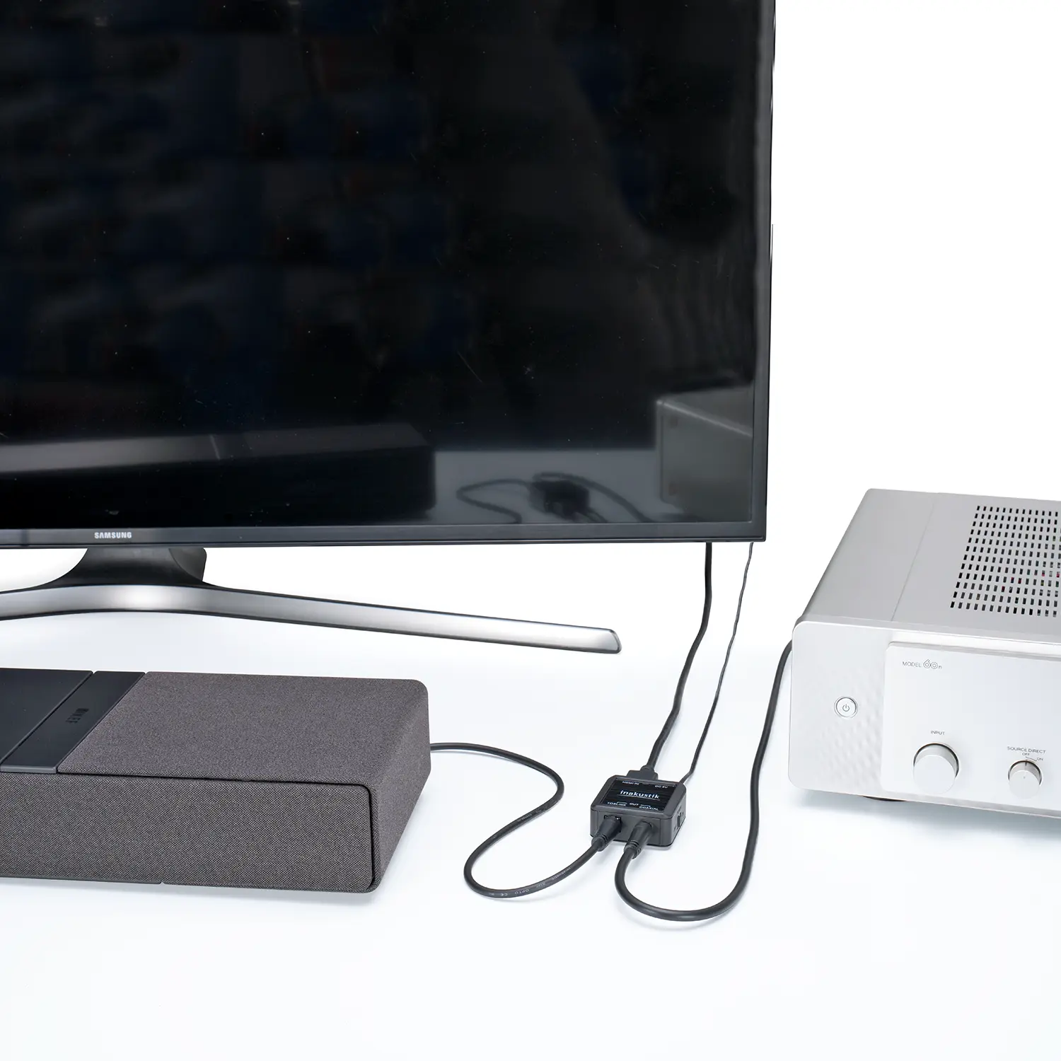 HDMI-Extractor mit angeschlossenen Kabeln zwischen einem Fernseher, einem grauen Lautsprecher und einem silbernen Verstärker auf weißem Untergrund